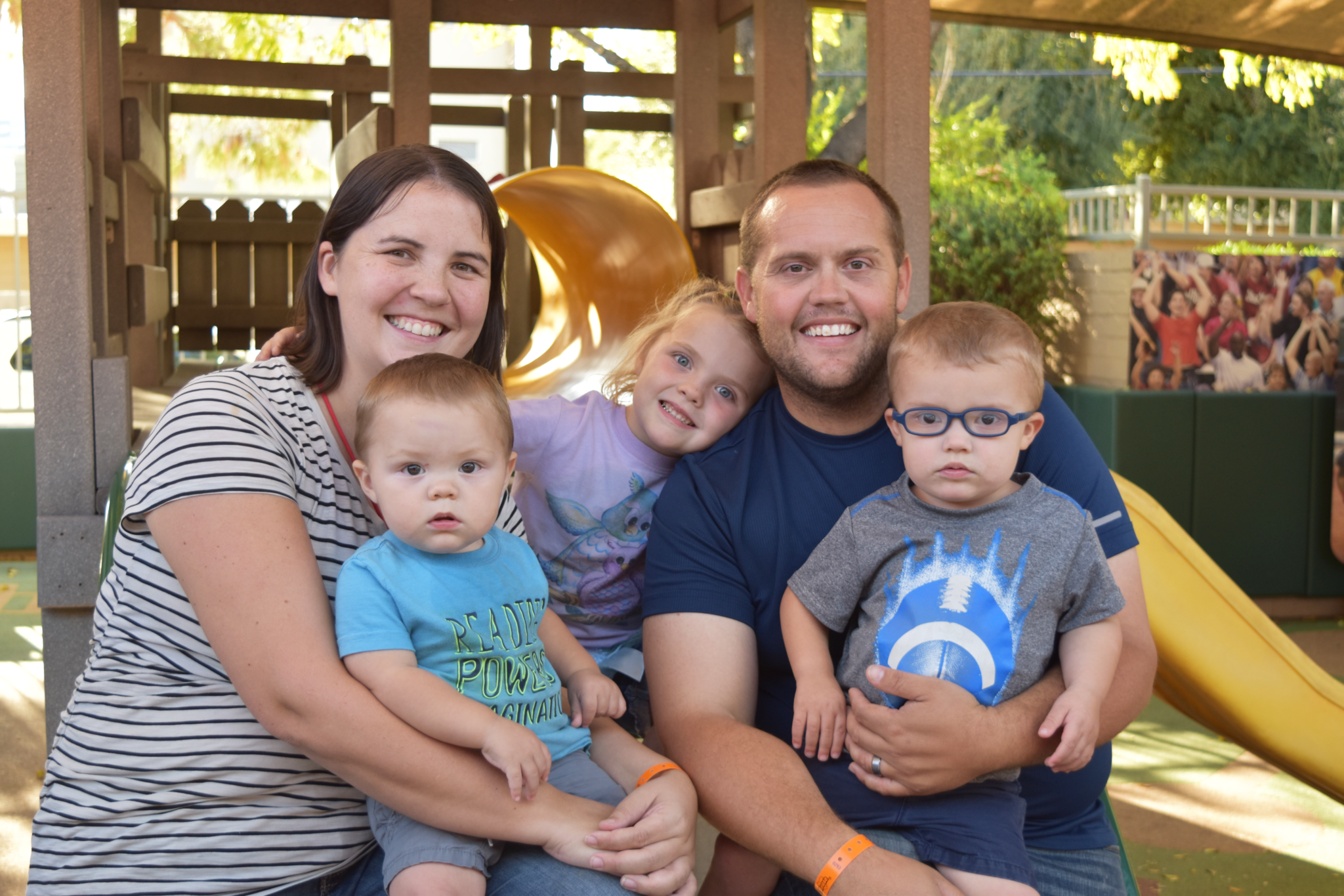 Mom, dad, sister, and two brothers huddle together on the RMHC playground.