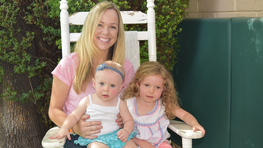 Mother sits in a rocking chair with her two daughters on her lap