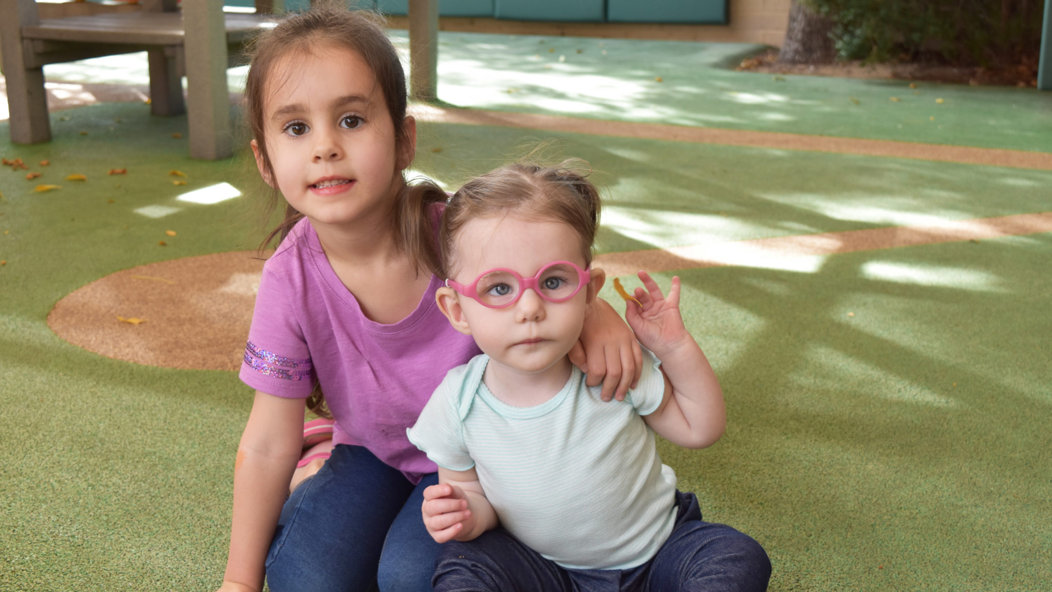 Older sister with her arm around her younger sister on the playground