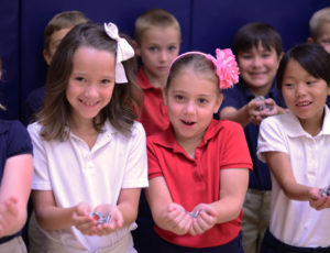 Young students in uniforms pose with pop tabs in their hands