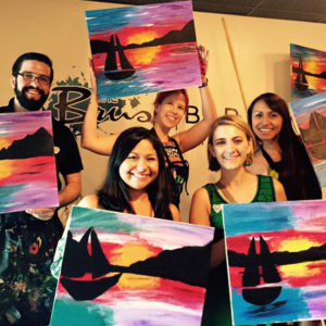 Group of Red Shoe Members pose with paintings they made at a Brush Bar fundraiser