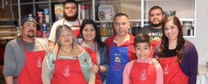 A family of volunteers pose in their RMHC aprons in the RMHC kitchen during dinner