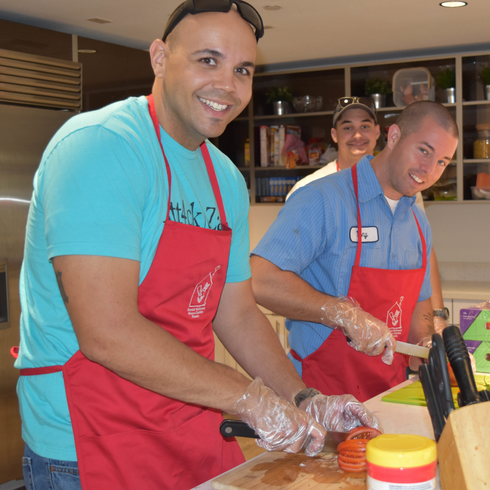 Two men with RMHC aprons cutting up vegetables in the kitchen